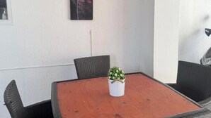 Een eetruimte met een houten tafel, rieten stoelen, een potplant en twee aan de muur bevestigde schilderijen.
