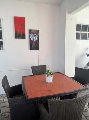 Ein Essbereich mit einem Holztisch, Korbstühlen, einem Blumentopf und zwei an der Wand befestigten Bildern.