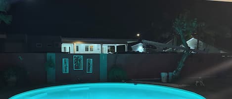 Una piscina con borde de baldosas de piedra, rodeada por un edificio de techo plano y una puerta visible.