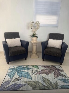 Zwei Sessel mit weißen Kissen, ein kleiner Tisch mit einer Orchidee im Topf und ein gemustertes Teppich auf Fliesen.