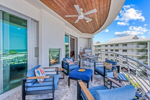 A balcony with outdoor furniture, a ceiling fan, and a view of a building complex. - NEW! Gulf View Paradise | Gulf Views, Shared Pool, Hot Tub, Exclusive Beach Access (Siesta Key)