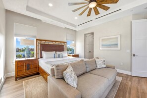 A bedroom with a bed, a wooden headboard, a nightstand, a window with blinds, a ceiling fan, a door, and a framed picture on the wall. - NEW! Gulf View Paradise | Gulf Views, Shared Pool, Hot Tub, Exclusive Beach Access (Siesta Key)