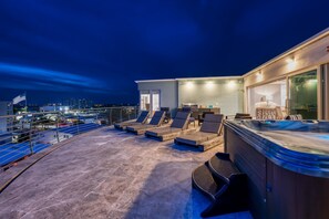 Eine Dachterrasse mit Liegestühlen, einem Whirlpool und Blick auf die beleuchtete Stadt.
