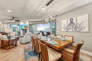 A modern dining area with a wooden table and chairs, a large window with a view of the ocean, and a ceiling fan. - NEW! Gulf View Paradise | Gulf Views, Shared Pool, Hot Tub, Exclusive Beach Access (Siesta Key)