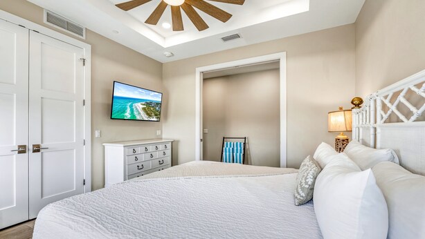 Een slaapkamer met een groot bed, een aan de muur bevestigde televisie, een plafondventilator en een nachtkastje met een lamp.