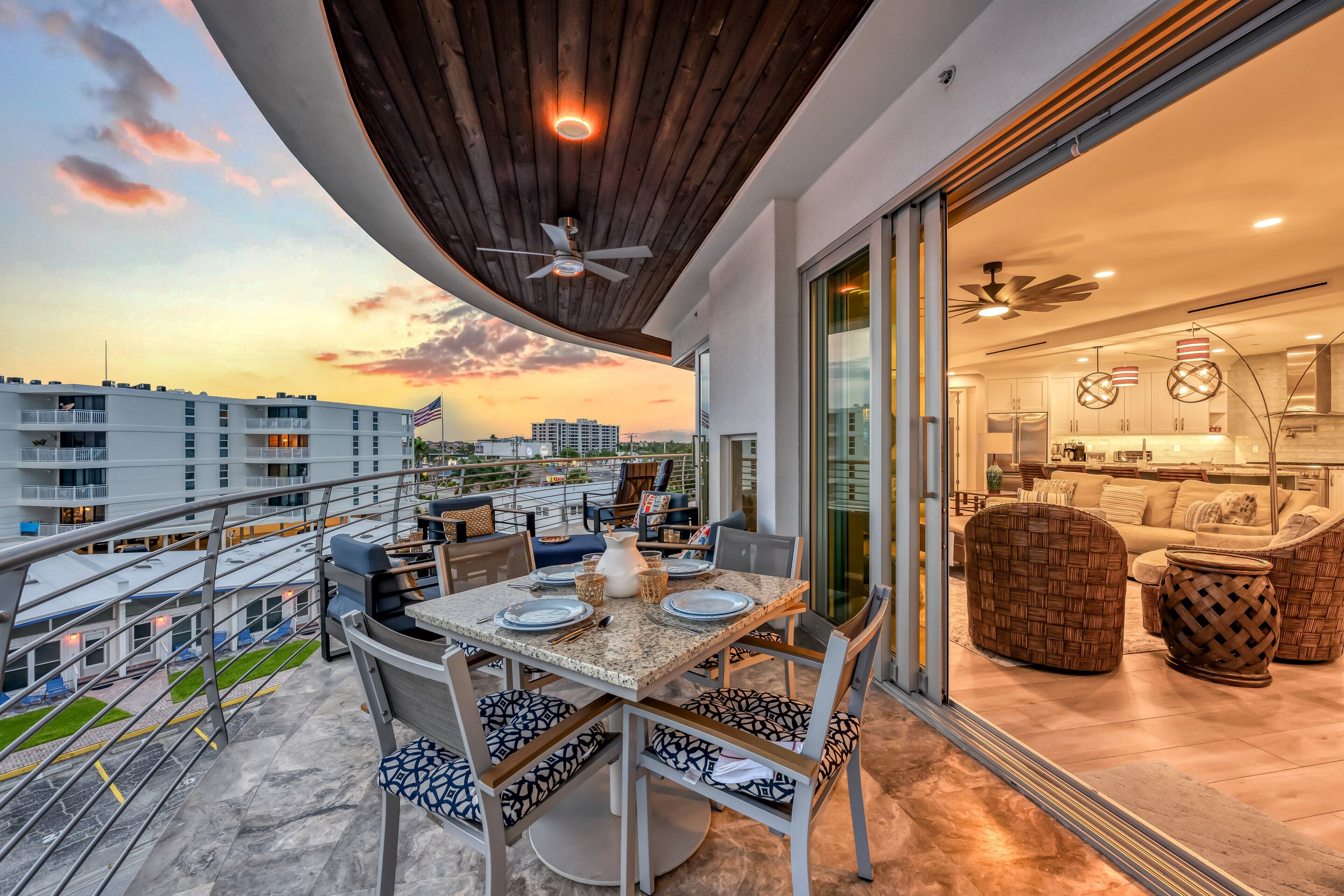A balcony with a dining table, chairs, and a view of the cityscape at sunset.