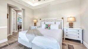 A bedroom with a large bed, two bedside tables with lamps, a ceiling fan, and a view into another room. - NEW! Gulf View Suite | Gulf Views, Shared Pool, Exclusive Beach Access (Siesta Key)