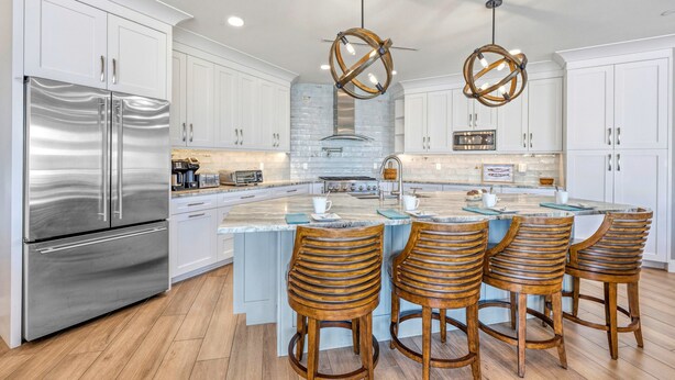 A modern kitchen with a stainless steel refrigerator, white cabinetry, a central island with bar stools, and pendant lighting. - NEW! Gulf View Suite | Gulf Views, Shared Pool, Exclusive Beach Access (Siesta Key)