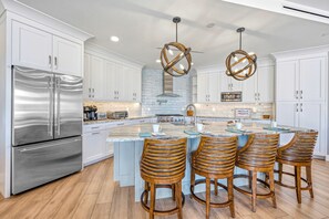 A modern kitchen with a stainless steel refrigerator, white cabinetry, a central island with bar stools, and pendant lighting. - NEW! Gulf View Suite | Gulf Views, Shared Pool, Exclusive Beach Access (Siesta Key)
