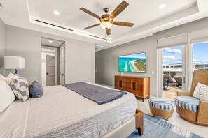 A bedroom with a bed, a ceiling fan, a TV, a balcony with outdoor furniture, and a view of the ocean. - NEW! Gulf View Penthouse | Gulf Views, Hot Tub, Top-Floor Balcony (Sarasota)
