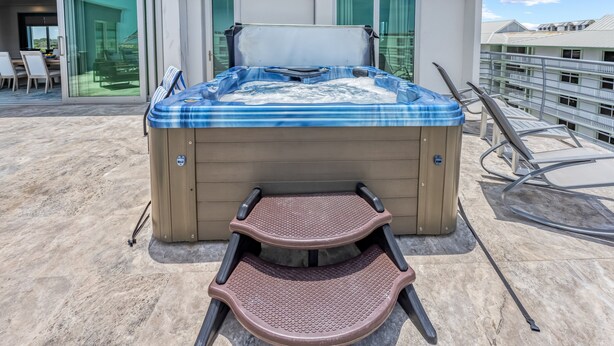 A hot tub with a footrest and a table, located on a deck with a glass door and a chair. - NEW! Gulf View Penthouse | Gulf Views, Hot Tub, Top-Floor Balcony (Sarasota)