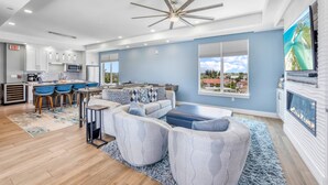 A spacious living room with a large TV, a fireplace, and a view of a coastal landscape. - NEW! Gulf View Penthouse | Gulf Views, Hot Tub, Top-Floor Balcony (Sarasota)