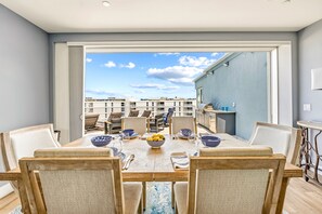 A dining area with a table set for four, chairs, and a view of a cityscape through a large window. - NEW! Gulf View Penthouse | Gulf Views, Hot Tub, Top-Floor Balcony (Sarasota)