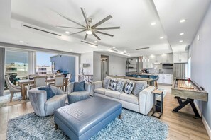 A modern living room with a sofa, ottoman, and a foosball table. - NEW! Gulf View Penthouse | Gulf Views, Hot Tub, Top-Floor Balcony (Sarasota)