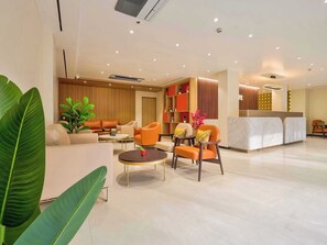 Un hall d’hôtel moderne comprenant un comptoir d’accueil, un espace salon avec des canapés et des fauteuils, et une grande plante.