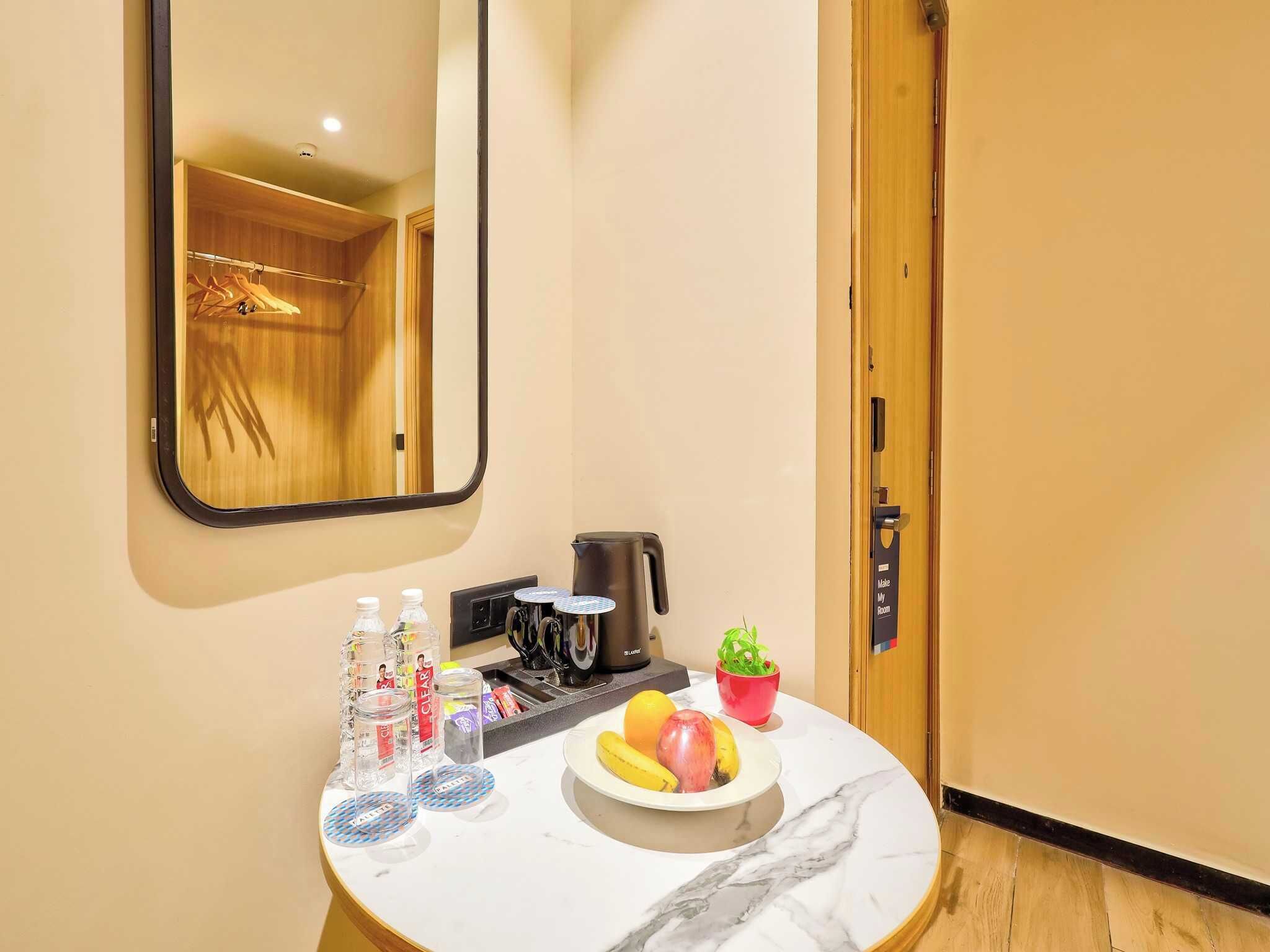 A hotel room with a marble countertop, a coffee maker, a fruit bowl, a potted plant, and a mirror.