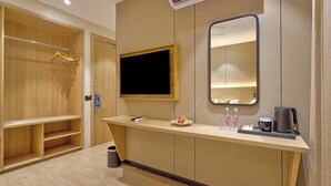 A hotel room with a wooden wardrobe, a flat-screen TV, a mirror, a small table with a fruit bowl, a kettle, and a trash bin. - Palette Convention Hotel Millennium City (Gurugram)