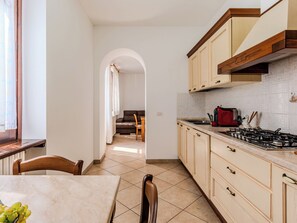 Una cocina con estufa a gas, alacenas y un comedor con mesa y sillas.