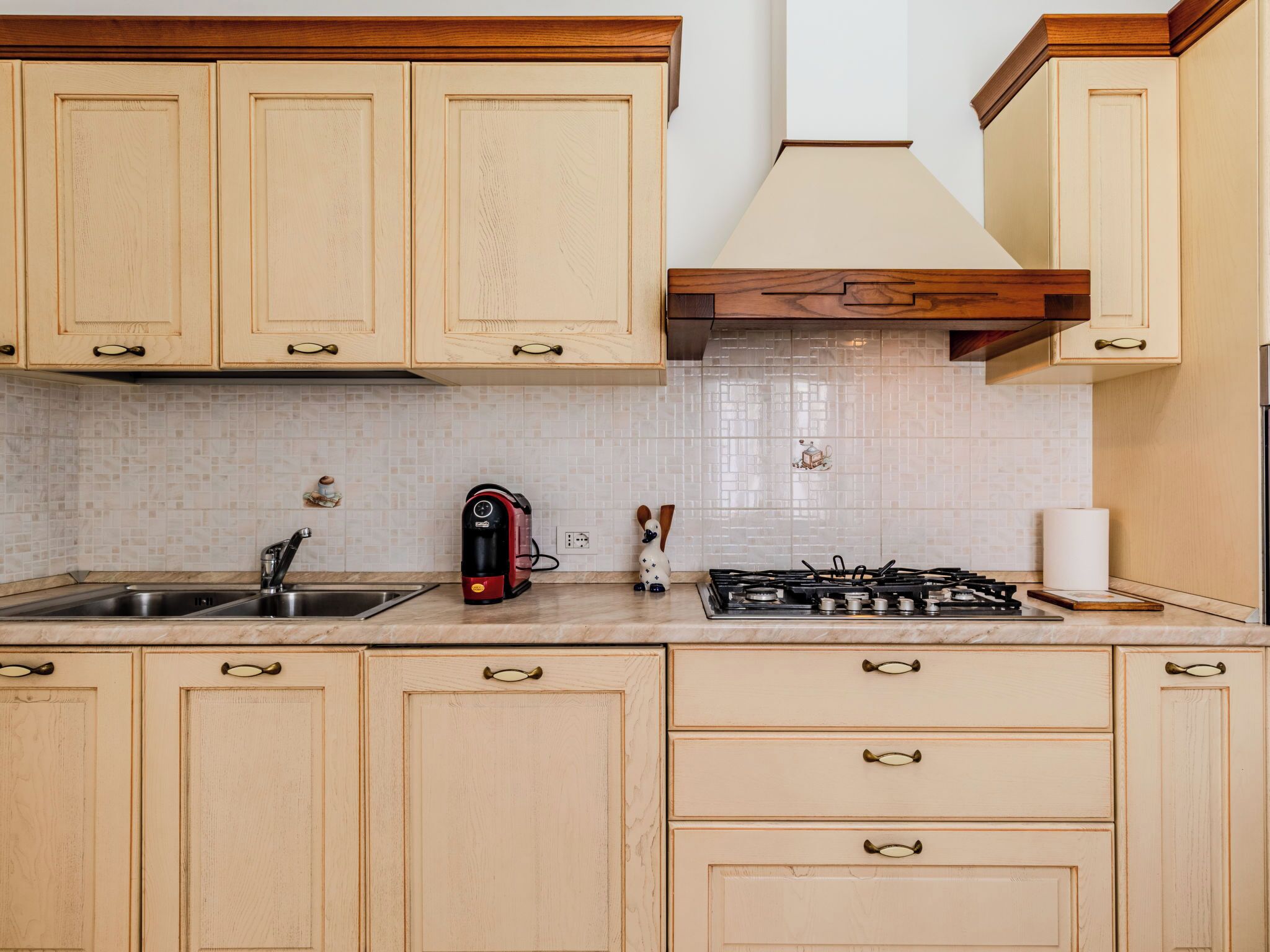 Une cuisine avec des meubles de rangement en bois, une cuisinière à gaz, une machine à café et un évier.