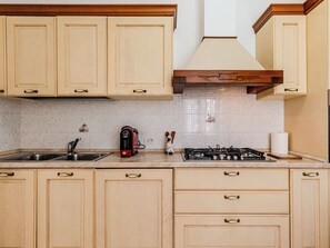 A kitchen with wooden cabinets, a gas stove, a coffee maker, and a sink. - Casa Iolanda by Interhome (Carlazzo)