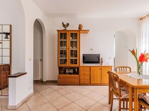 A dining area with a wooden table, chairs, a cabinet with glass doors, a television, and a vase with flowers. - Casa Iolanda by Interhome (Carlazzo)