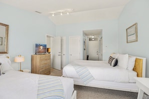 A hotel room with two beds, a dresser, a desk, and a mirror. There is a door leading to a hallway.