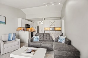 A modern living room with a grey sofa, a white coffee table, and a grey armchair.
