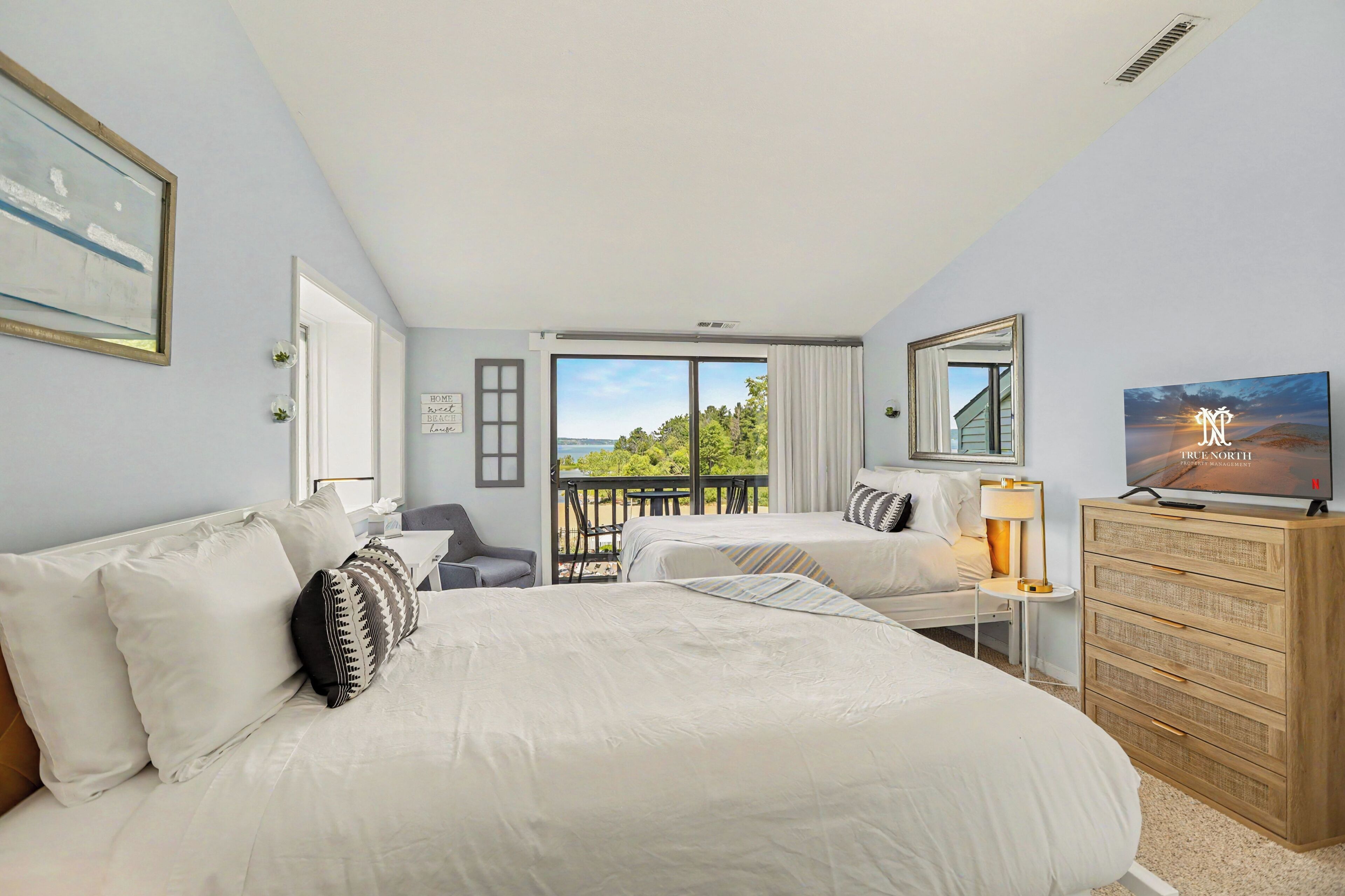 A hotel room with two beds, a desk, a dresser, and a balcony with a view.