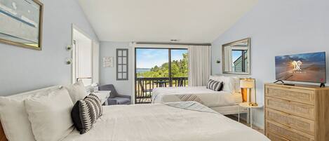 A hotel room with two beds, a desk, a dresser, and a balcony with a view.