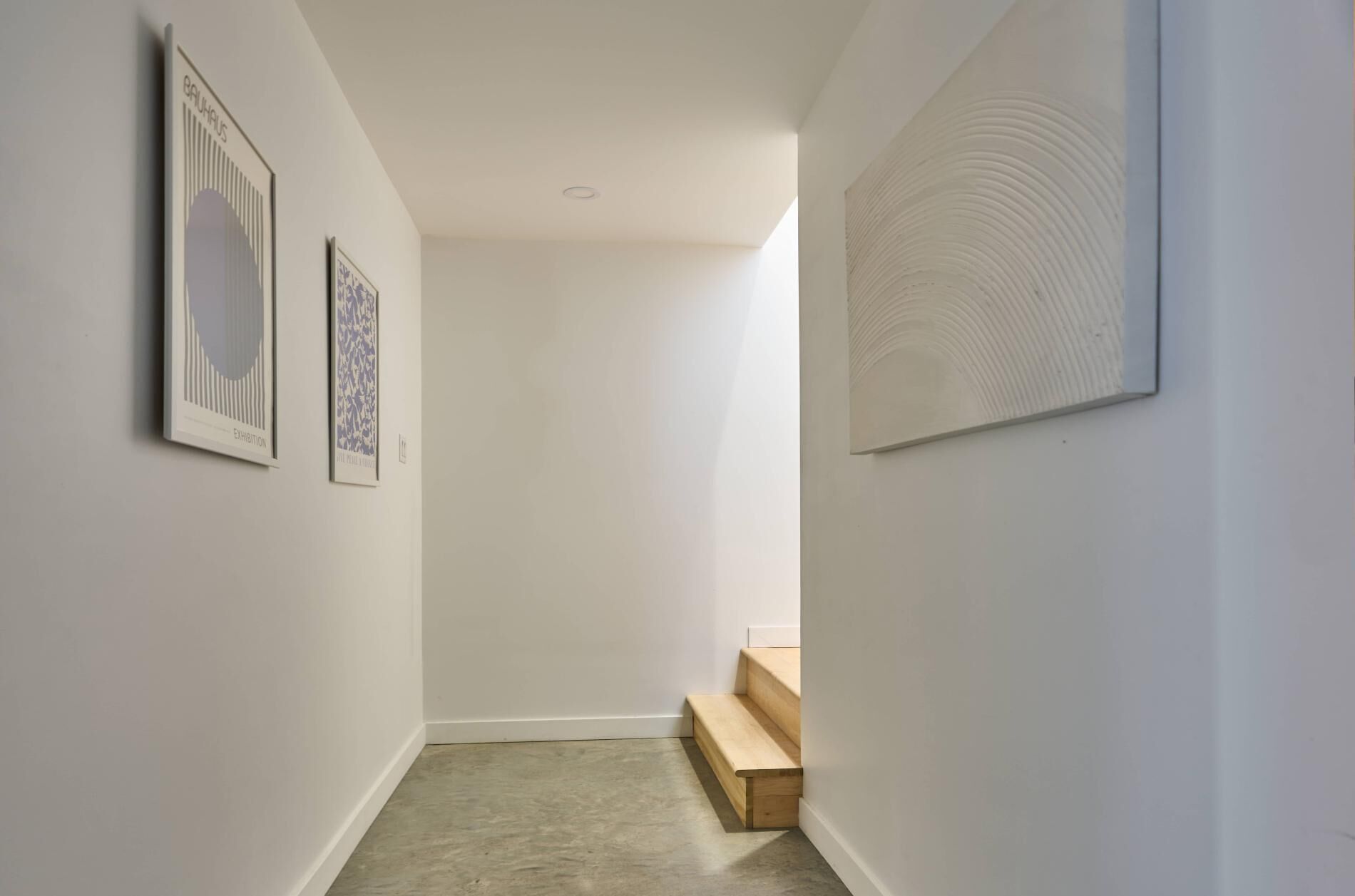 Un couloir aux murs blancs, avec un banc en bois et deux œuvres d’art encadrées.