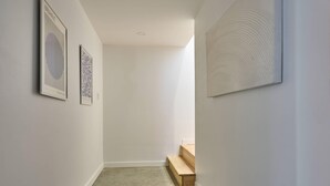Un pasillo con paredes blancas, un banco de madera y dos cuadros enmarcados.