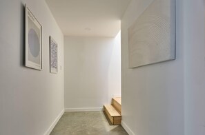A hallway with white walls, a wooden bench, and two framed artworks.