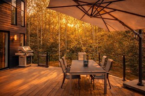 A wooden deck with a table and chairs, a grill, and a large umbrella.