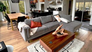 Una sala moderna con un sofá gris, una mesa de centro de madera y un comedor con mesa y sillas de madera.