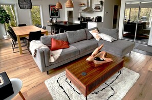 En moderne stue med en grå sofa, et træbord som sofabord, og et spiseområde med et træbord og stole.