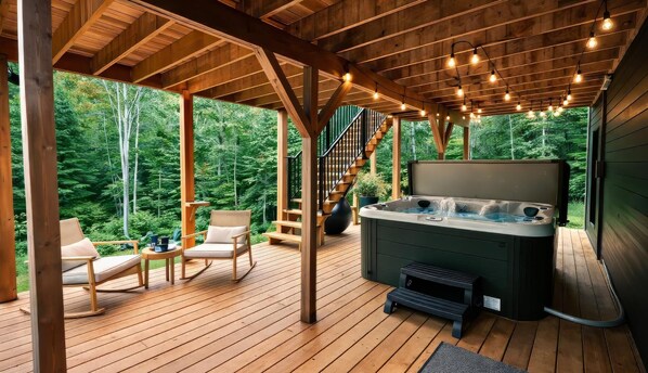 A wooden deck with a hot tub, chairs, and a staircase leading to an upper level.