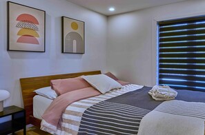 Ein Schlafzimmer mit einem Bett, Kissen, einer Decke, einem Nachttisch und zwei Wandbildern.