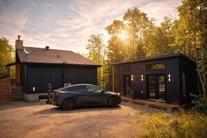 A modern two-story house with a car parked in front, surrounded by trees.