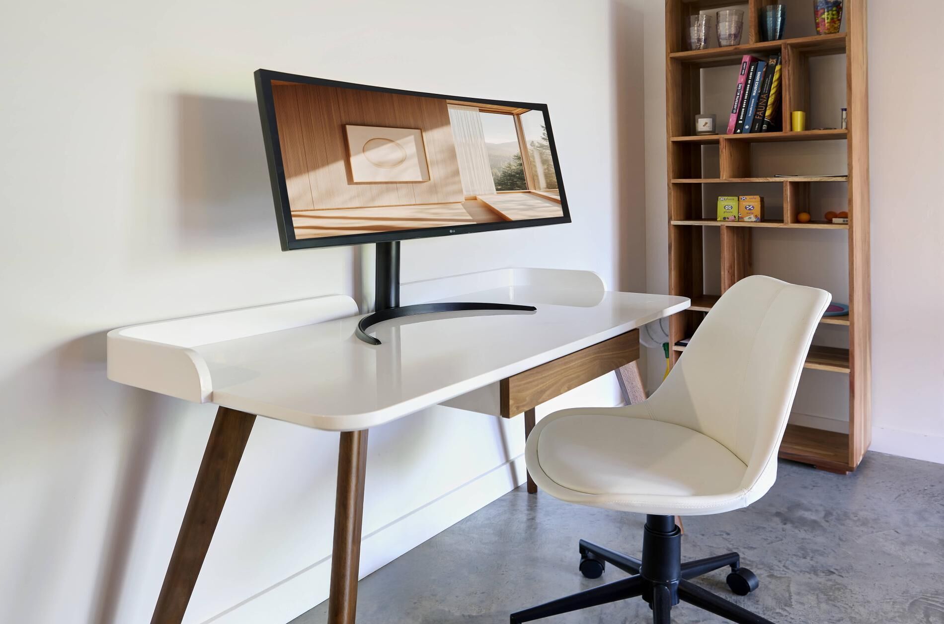 A modern office desk with a computer monitor, a white chair, and a wooden bookshelf in the background.