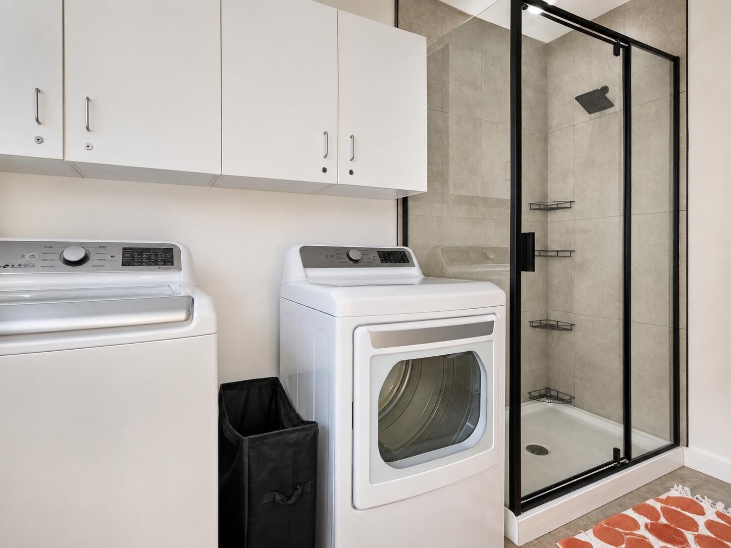 A laundry room with two washing machines, a dryer, and a glass-enclosed shower area.