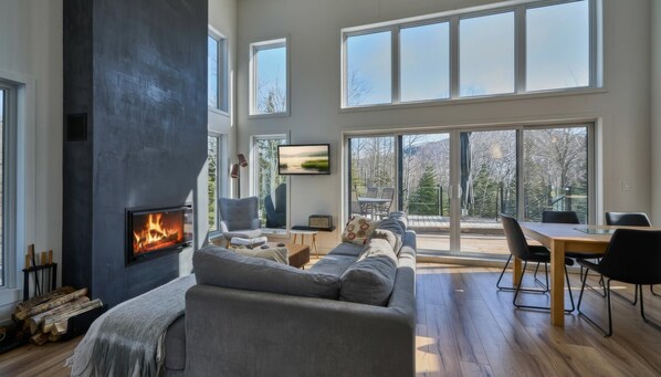 A modern living room with a fireplace, large windows, and a view of the outdoors.
