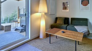 Un interior moderno con un ventanal corredera que da a un espacio exterior, una lámpara de pie, un conjunto de sofás y dos cuadros enmarcados en la pared.