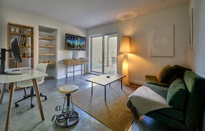 Una sala de estar moderna con un sofá, un escritorio, una silla, una estantería, un televisor y una lámpara.