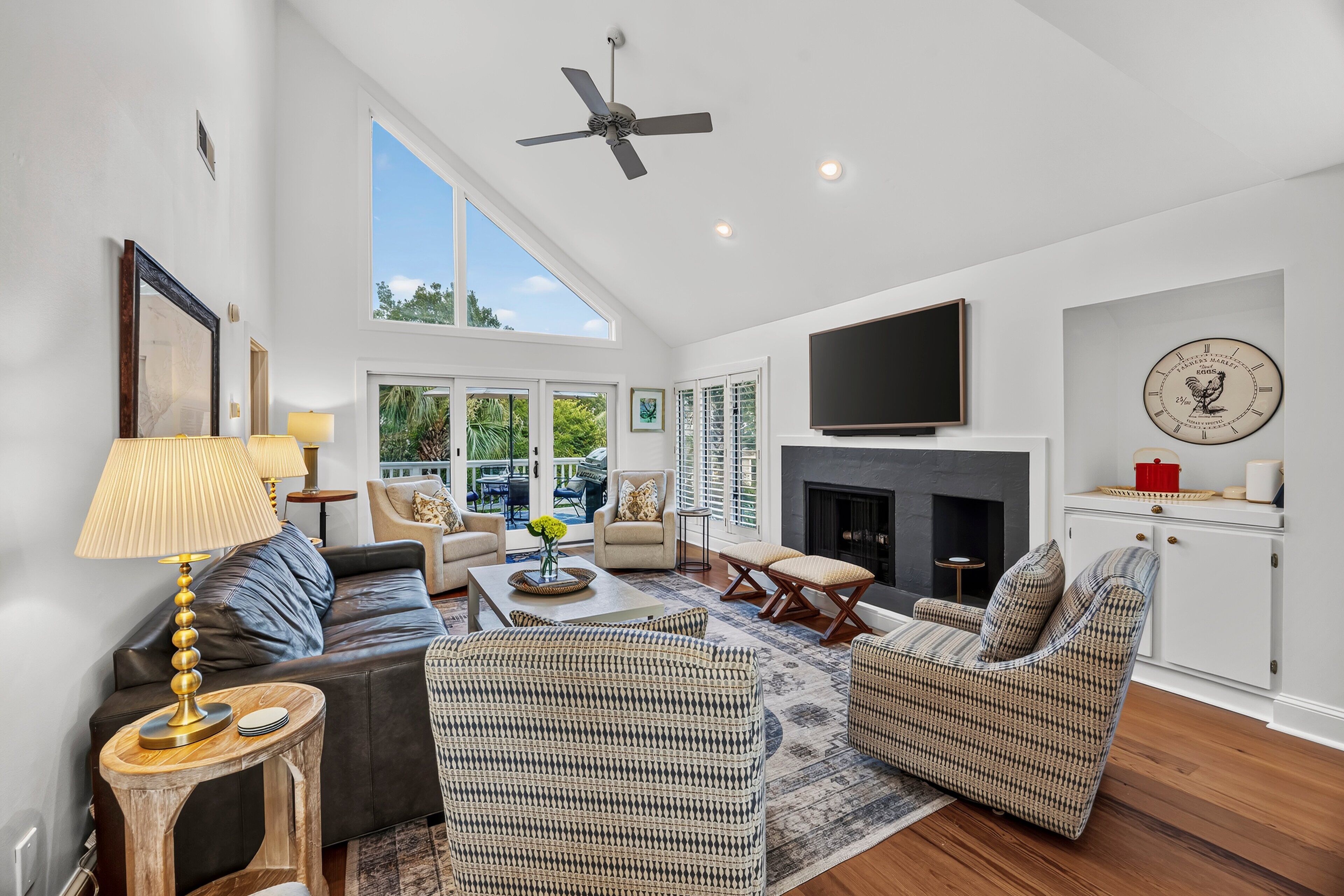 A spacious living room with a fireplace, a flat-screen TV mounted above it, and a ceiling fan.