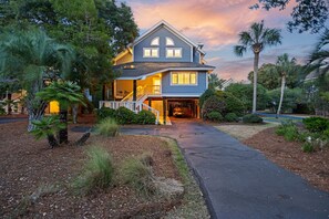 Ein zweistöckiges Haus mit überdachter Garage, umgeben von einem angelegten Garten mit Palmen und Sträuchern.