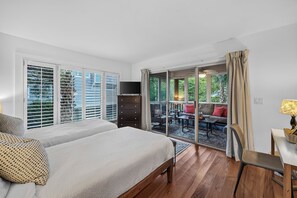 Ein Schlafzimmer mit einem großen Bett, einem Schminktisch und einem Fernseher. Eine Glastür führt auf einen Balkon mit Gartenmöbeln.