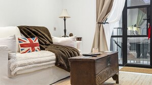 A living room with a sofa, a lamp, a wooden side table, and a view through a glass door. - Pet Friendly Studio in Fulham, Sleeps 2 (London)