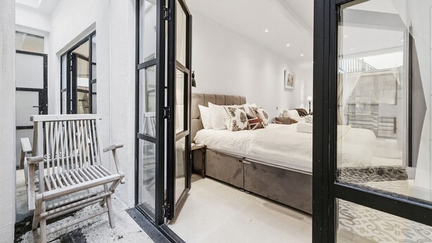 A bedroom with a bed, a bench, and a glass door leading to a balcony. - Pet Friendly Studio in Fulham, Sleeps 2 (London)