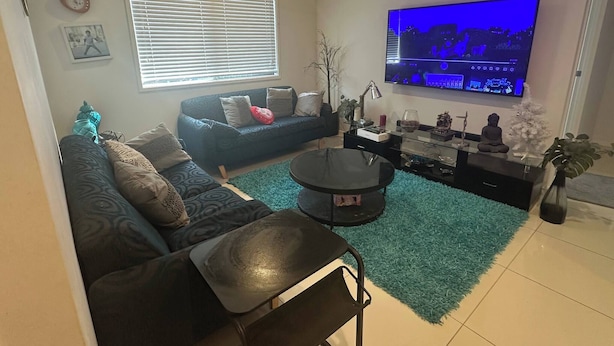 A living room with a sofa, a coffee table, a TV, and a plant. - Room-our Little World in Caloundra (Sunshine Coast)