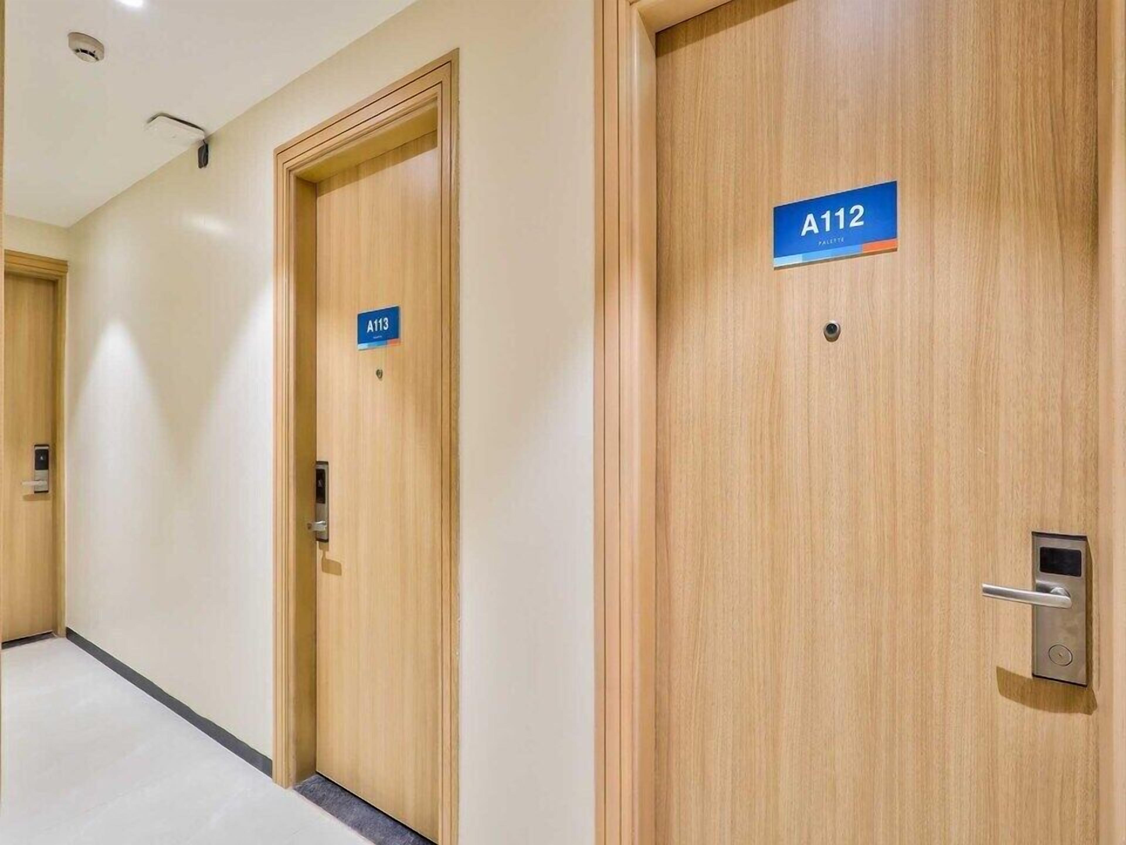 A hotel corridor with wooden doors, each marked with a room number sign.